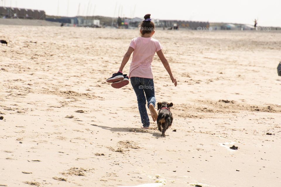 Little girl running with the dog on the beach