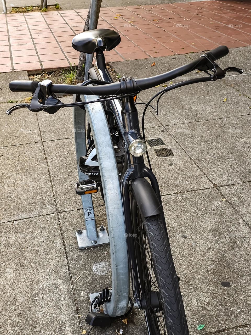 Black bicycle chained up on the streets of San Francisco, sleek with the safety helmet strapped to its side 