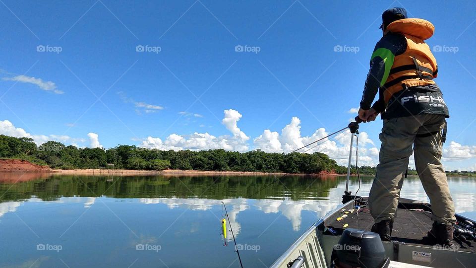 Um pescador no barco, céu azul nublado e águas tranquilas.