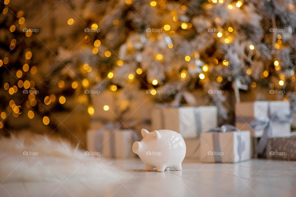 piggy bank with 100 dollars banknote in festive New Year atmosphere of scenery.  Magical bokeh with Christmas tree and bright lights.