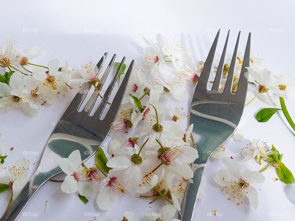 Two metal forks on the white table decorated with white flowers.  Close up