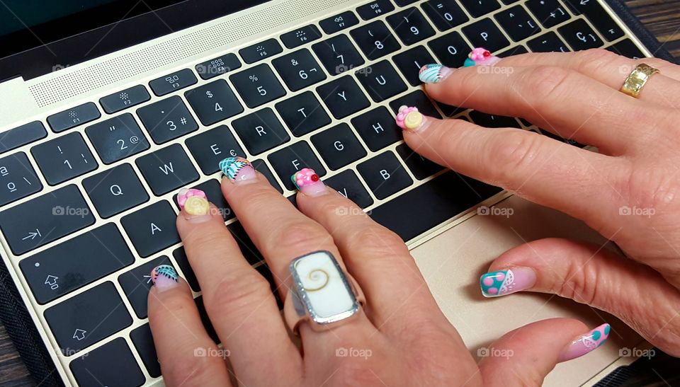 Woman with fancy nails working on her laptop.