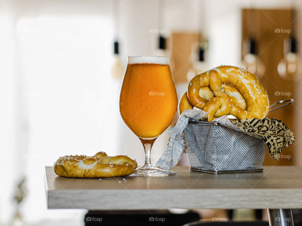 A glass of beer next to a couple of fresh backed pretzels