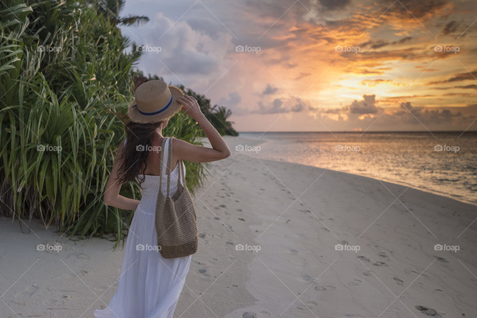 Girl in white dress and hat looking at the sunset
