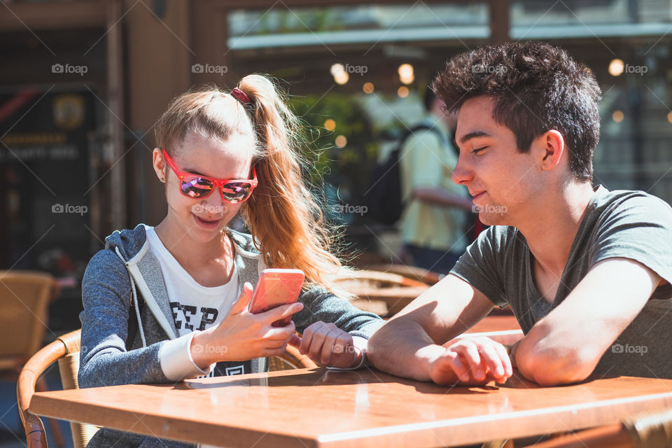 Young woman and man sitting in pavement cafe a the table talking and using mobile phones