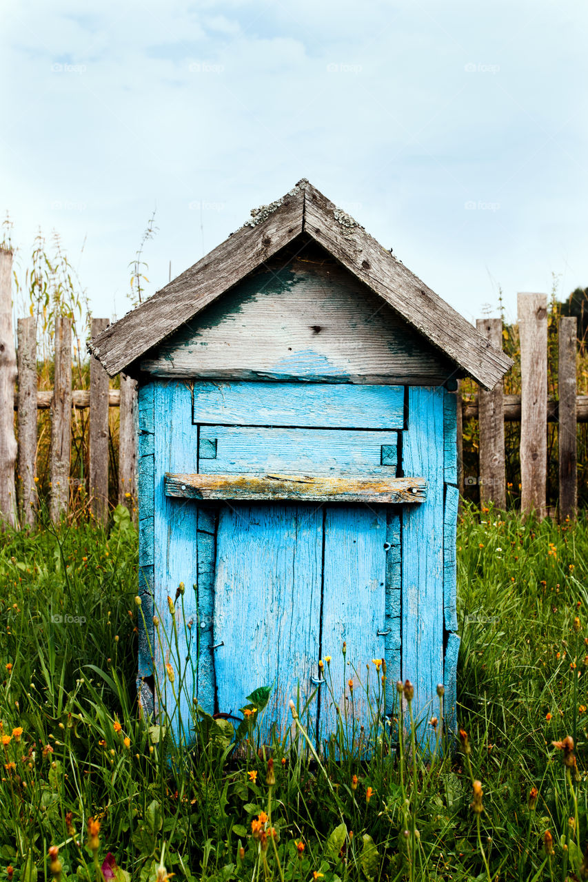 Old wooden hive painted in blue standing in the grass in home garden in the countryside