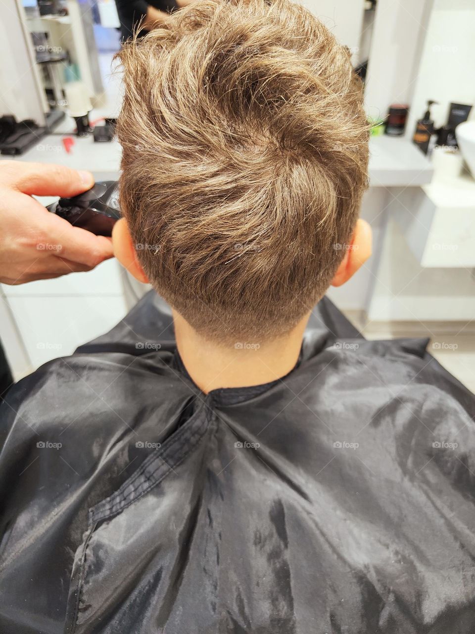 hairdresser performs a cut on a boy with electric hair clipper