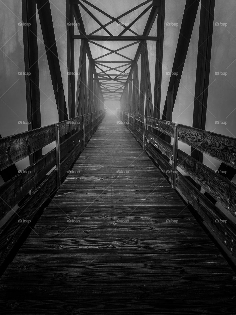 Black and white of an old steel and wood truss footbridge across the lake at Tims Ford State Park in Winchester Tennessee. The dark and foggy ambiance gives it a haunting and mysterious feel. 