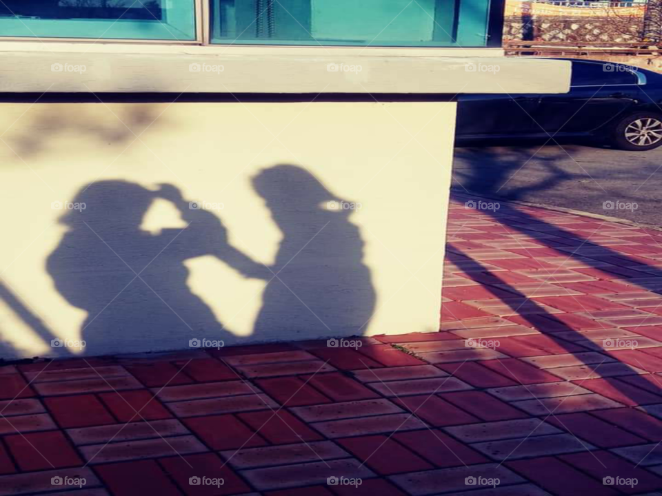 a shadow of a child standing in front of the mother and a mother is fixing her hair that covers her eyes because  of the wind.