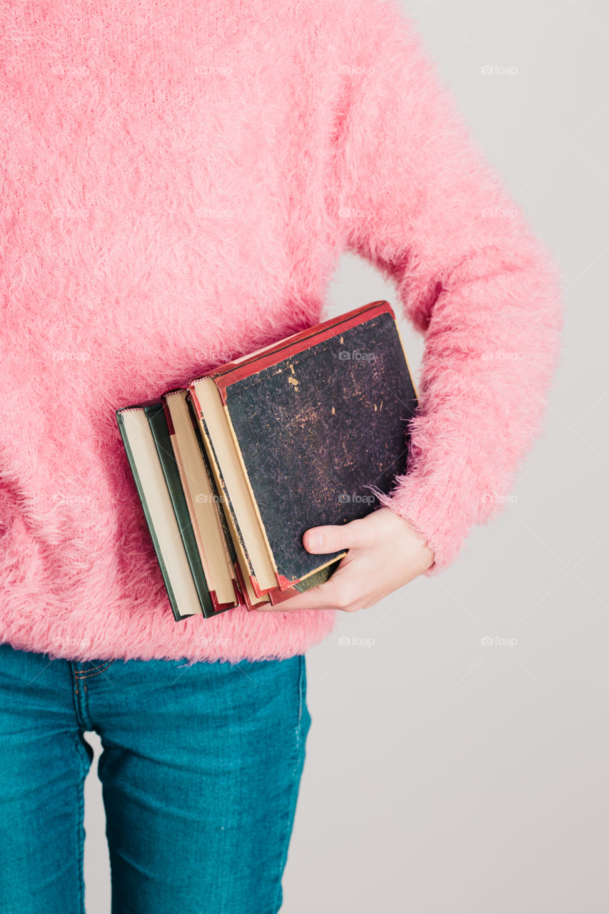 Young girl holding a few books. Teenager girl wearing pink sweater and blue jeans. Vertical photo