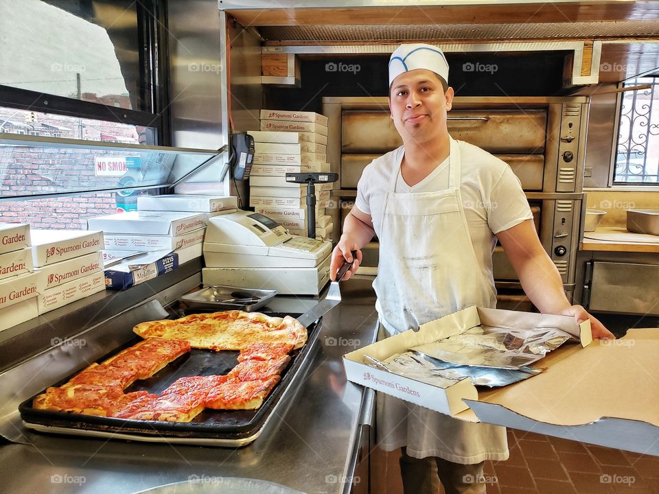 Chef cuts slices of Sicilian and Neapolitan pizza in a pizzeria