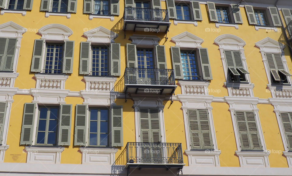 Bright yellow building with many irnate windows and French shutters on the Place Garibaldi in Nice, France.