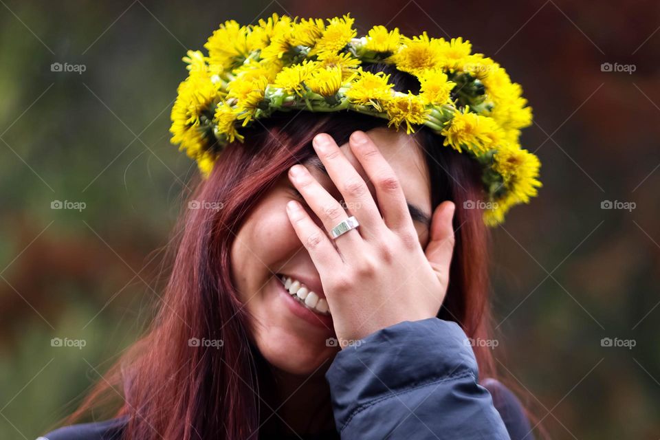 Beautiful young woman in a dandelion wreath is laughing covering her face with her hand