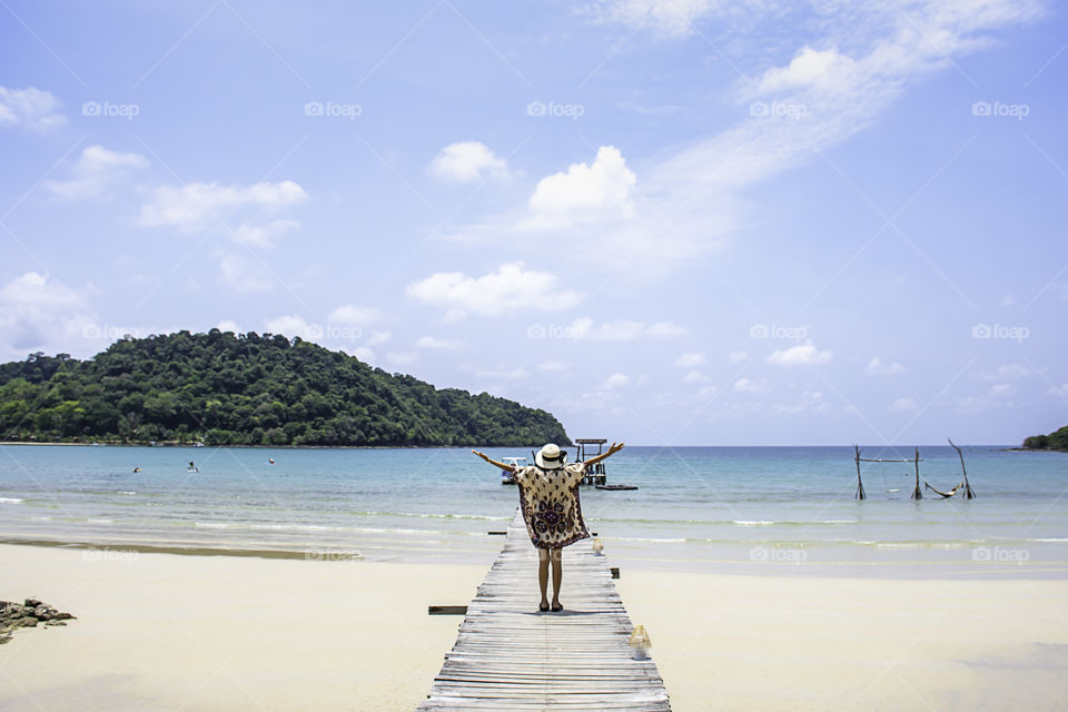 Women raise their arms and  wear a hat on the wooden bridge pier boat in the sea and the bright sky at Koh Kood, Trat in Thailand.