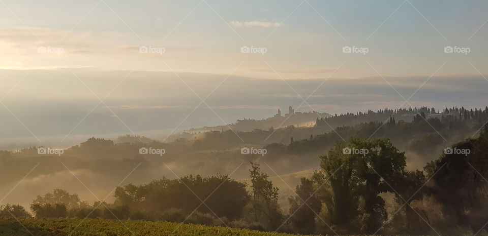 Early morning landscape over the Tuscan countryside with the towers of San Gimignano visible through the mist.