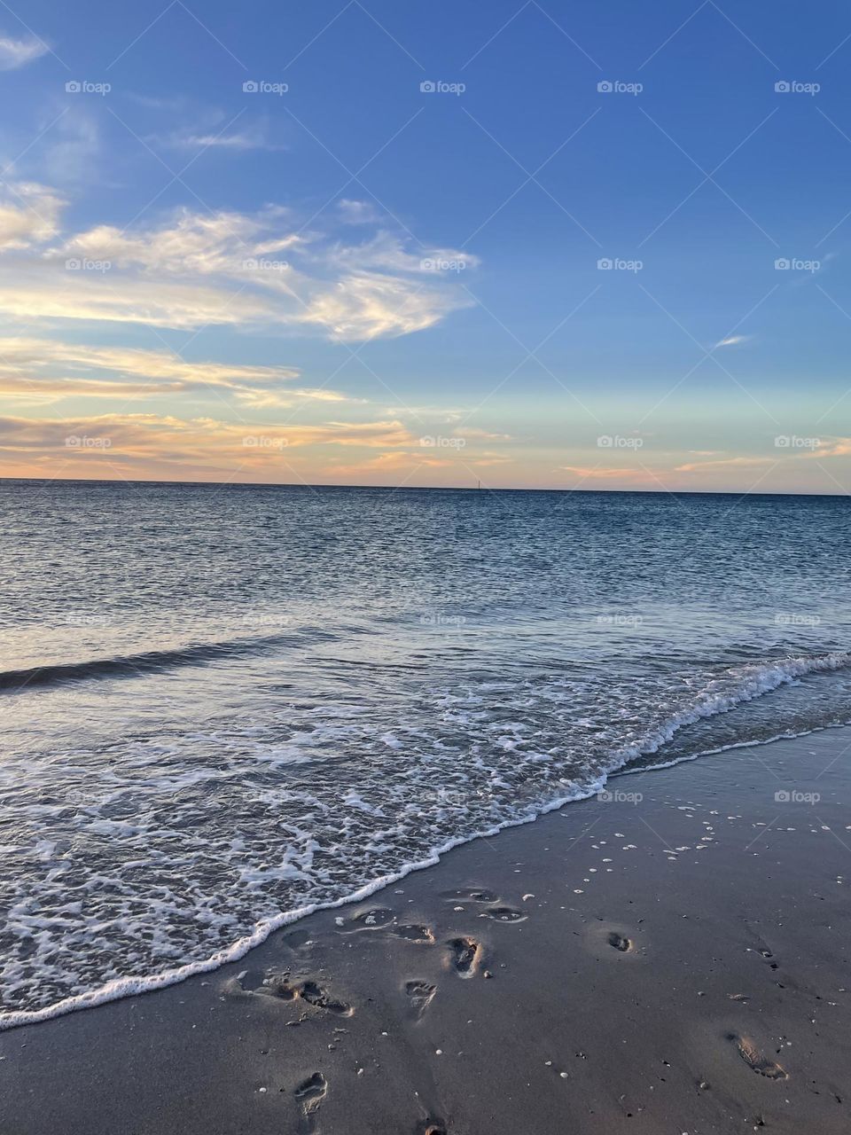 An Australian shoreline with footprints in the sand, still water and a faint sunset.