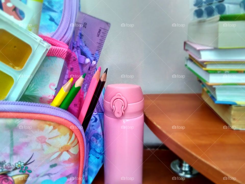collection of school supplies in a backpack, books lying on the table and a student's thermo mug
