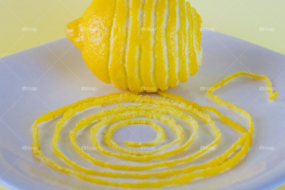 Lemon and spiraled lemon peel on a white plate with yellow background  