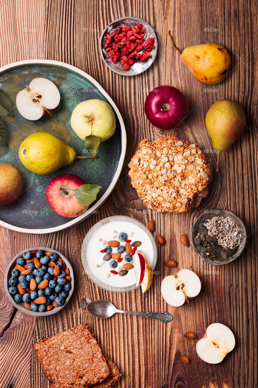 Breakfast on table. Yogurt with added blueberries and roasted almonds. Muesli cookie, apples and pears on wooden table. Light and healthy meal. Good quality balanced diet. Flat top-down composition