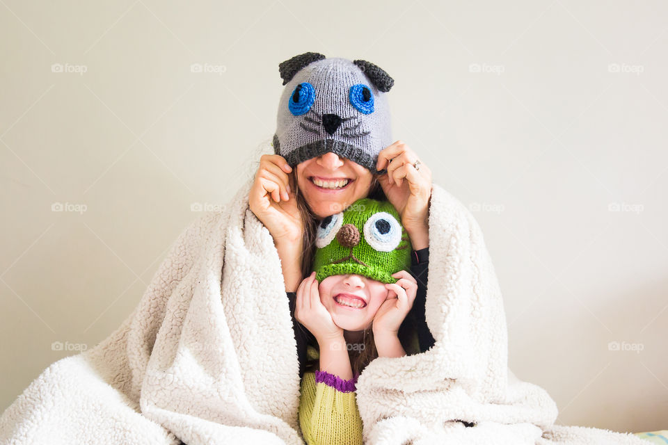 Winter fun and cuddles - image of mom and daughter laughing and having fun with animal beanies in a cozy winter blanket.