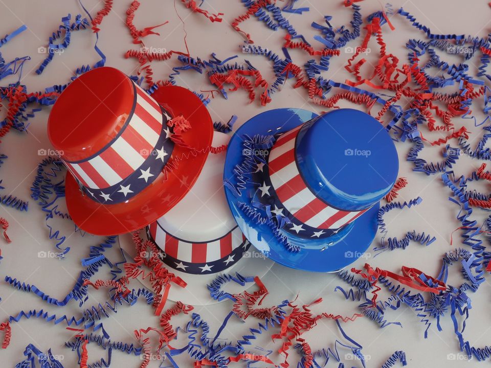 Tiny party hats in red, white, and blue with the Stars and Stripes for hat bands on a table with confetti. 