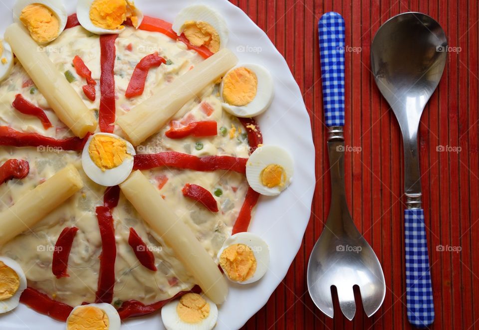 Dish of Russian salad cooked in the Spanish way.  Diced potatoes, carrots, peas and green beans with boiled egg, tuna, asparagus, red pepper and mayonnaise.