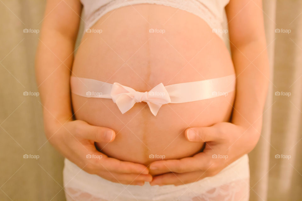 Close up image of pregnant woman tummy with pink ribbon 