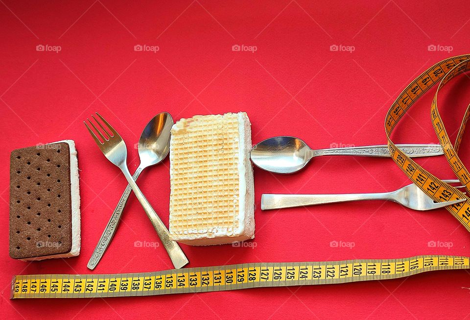 Rectangles.On a red background lies of ice cream with chocolate waffles and of ice cream with white waffles.Between the ice cream lie a crossed fork and spoon.Behind the white ice cream lie a fork and a spoon in the shape of an inverse proportional