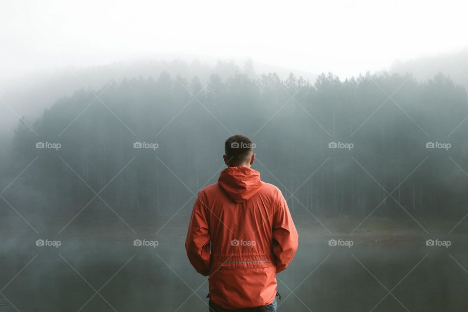 Man standing at lake during foggy weather.