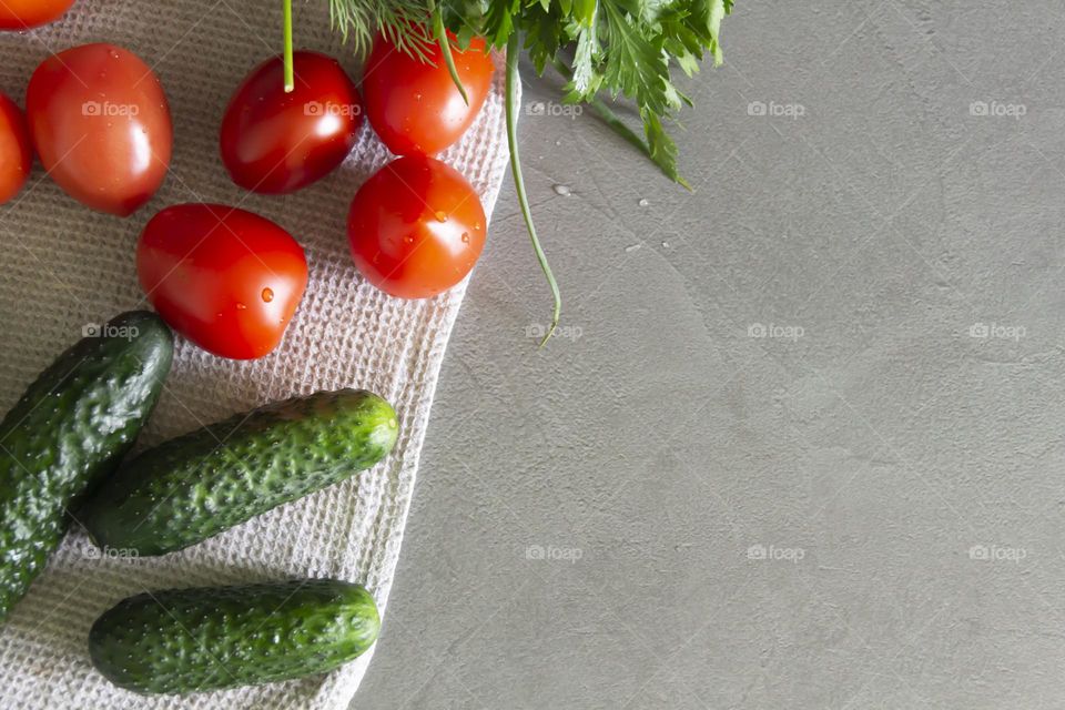 Fresh, bright, juicy vegetables and herbs for preparing salads and other vegetable dishes, are in a linen towel on a gray, kitchen work surface.