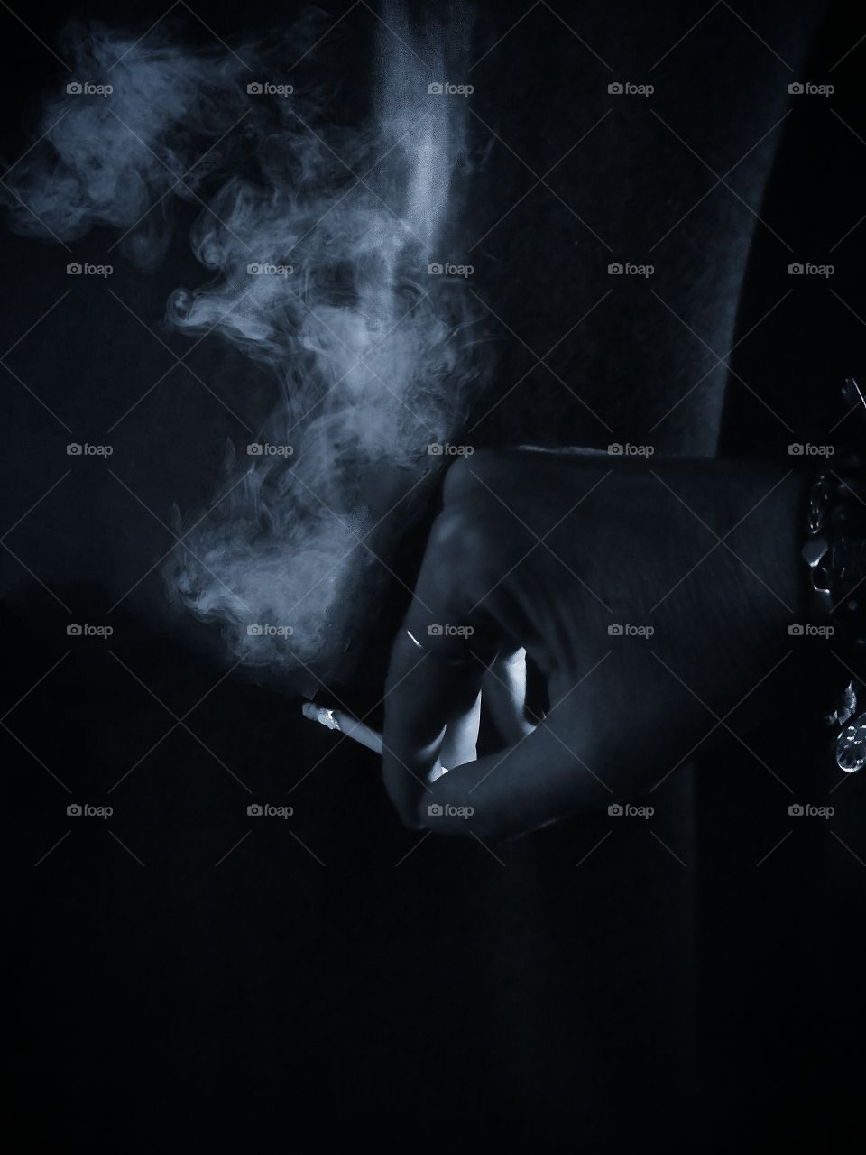 Hand holds a lit cigarette.  White smoke from cigarette background silhouette of a man