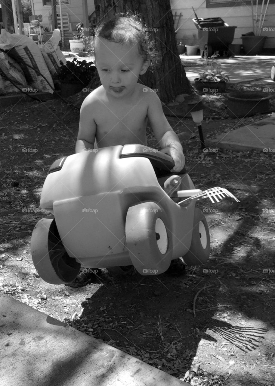 Barrier negotiation. A toddler puts all his effort into moving his rolling cart over the top of a barrier. 