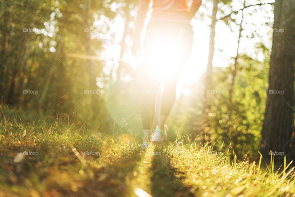 Crop photo of Young slim woman brunette in sport clothes running at forest on golden hour sunrise time. Health and wellness, fitness lifestyle