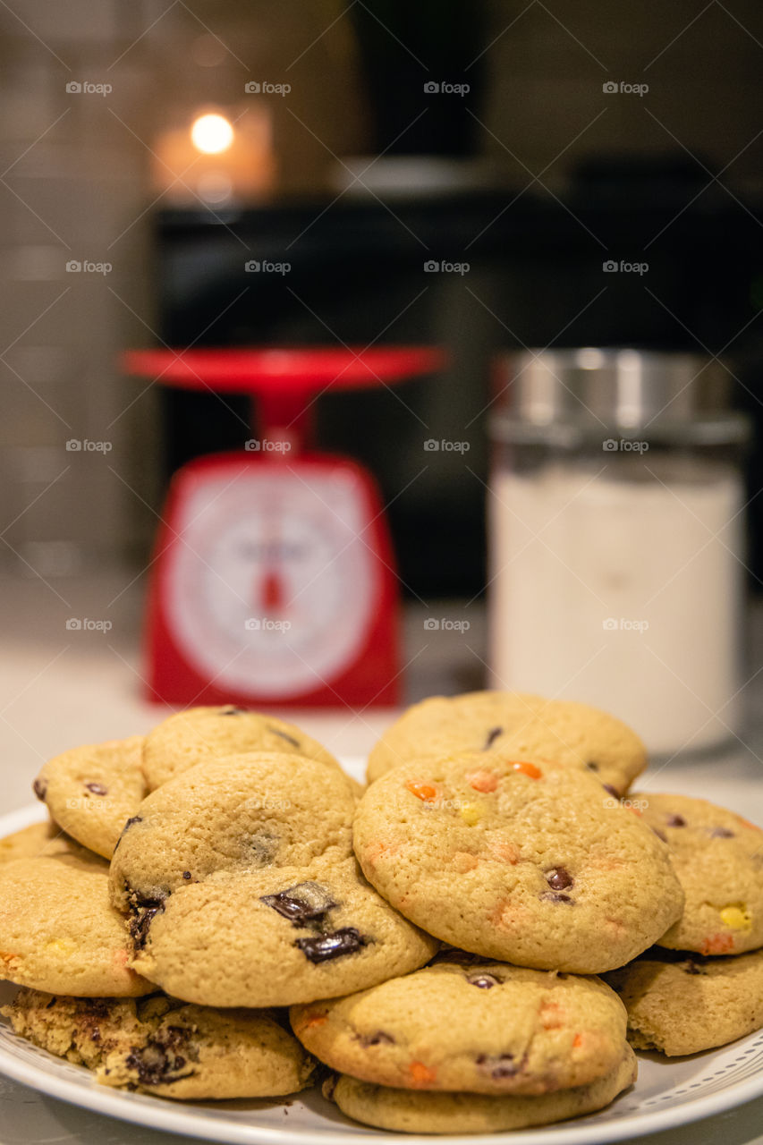 Chocolate chip cookies on a circular dish, with flour and a food scale in the background. Shallow depth of field. 