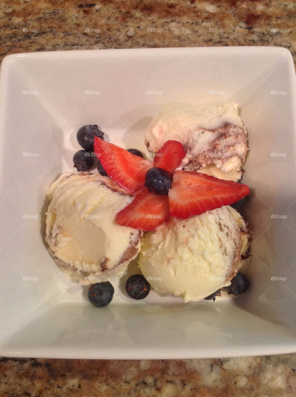 A photo of Vanilla ice cream with strawberries and blueberries. 