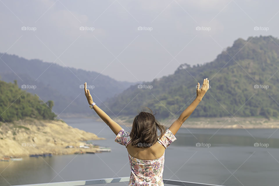 Women raise their arms Background mountains and water at Khun Dan Prakan Chon Dam ,Nakhon Nayok in Thailand.