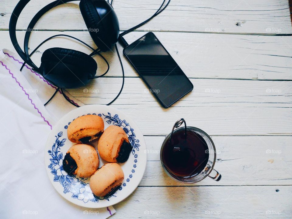 cup of tea, cakes, smart phone and headphones