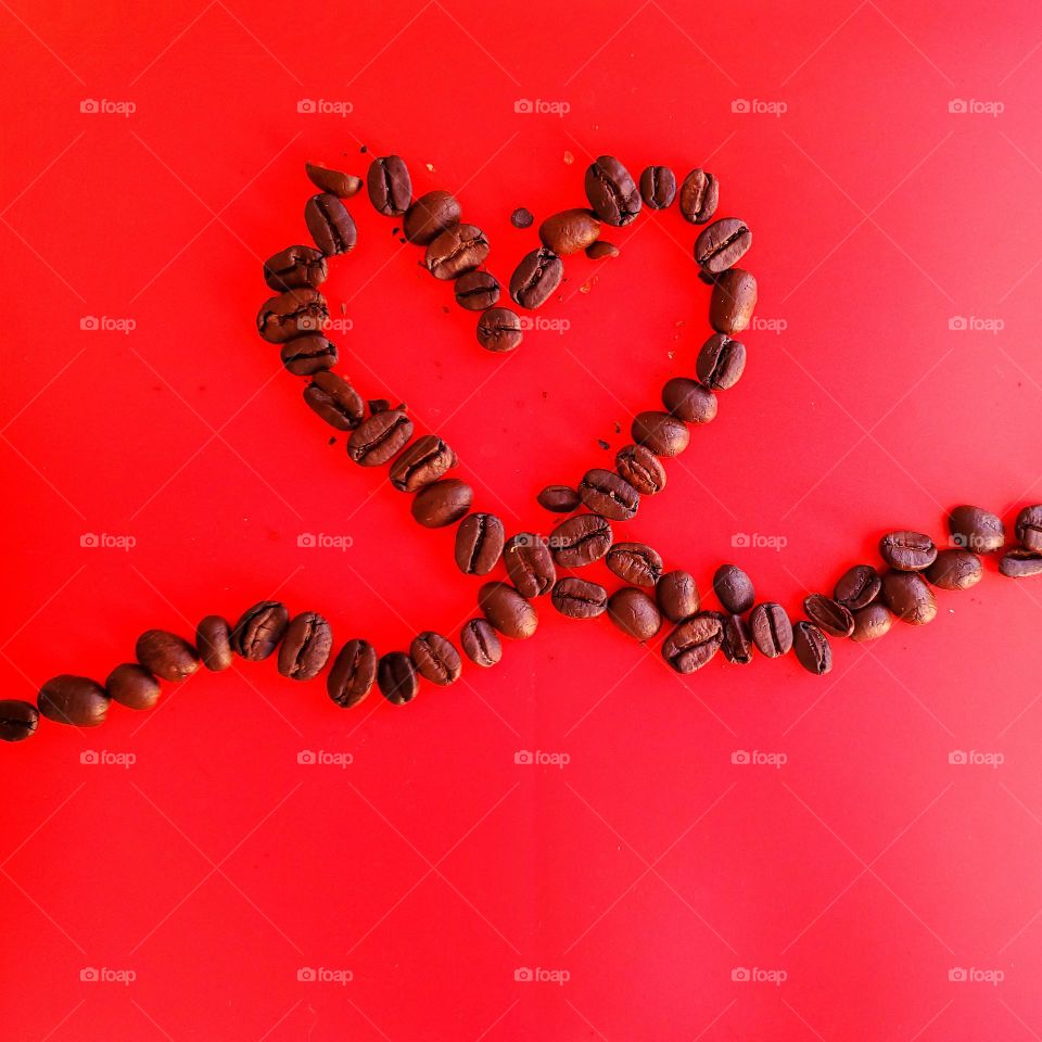 Coffee beans in a heart design on a red background.