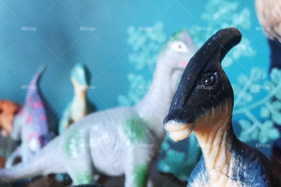 Toy plastic parasaurolophus dinosaur macro shot with other plastic dinosaurs and trees in the background