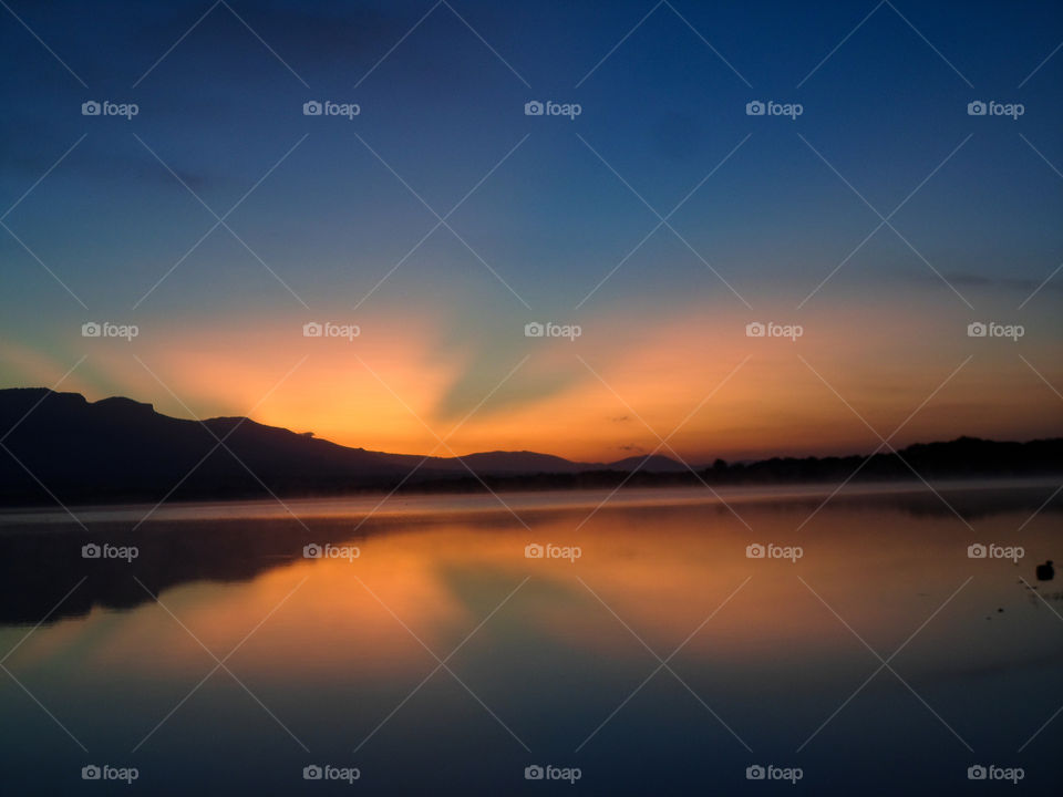sunset behind a mountain range with reflections on the still water