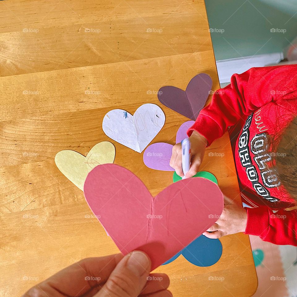 Toddler making Valentine’s Day hearts, child doing crafts indoors, craft time indoors in the winter time, winter time children’s crafts, making valentines, toddler playing with paper hearts, making Valentines Day decorations with a toddler 