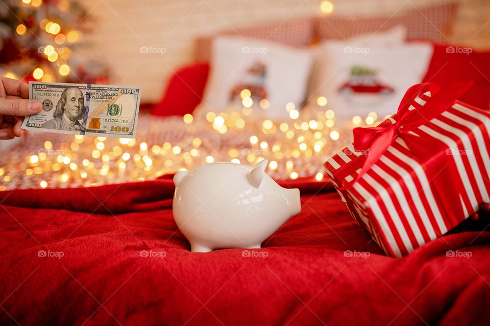 piggy bank with 100 dollars banknote in festive New Year atmosphere of scenery. Magical bokeh with Christmas tree and bright lights.