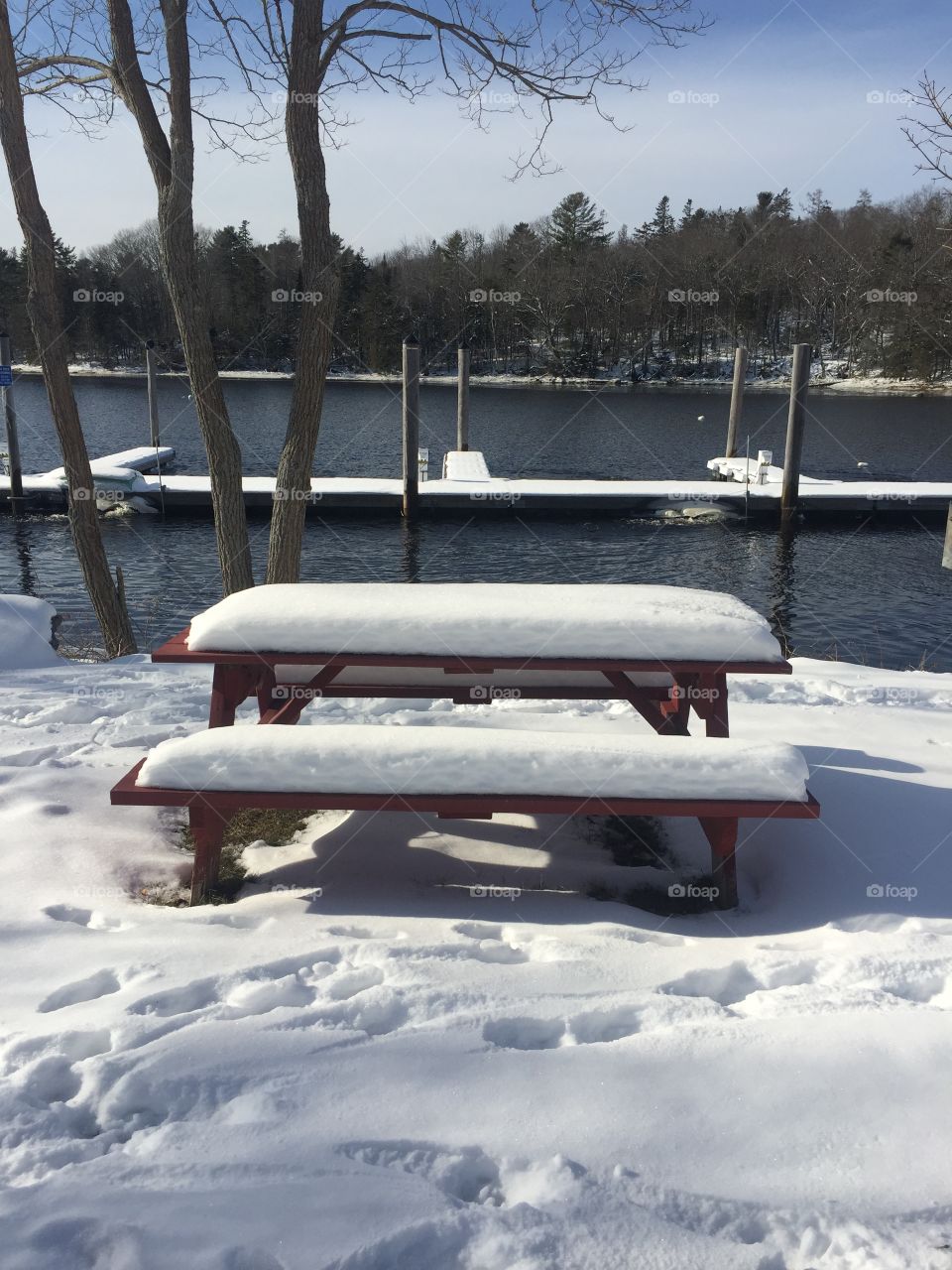 A snow covered picnic table in a park by the waterfront. 