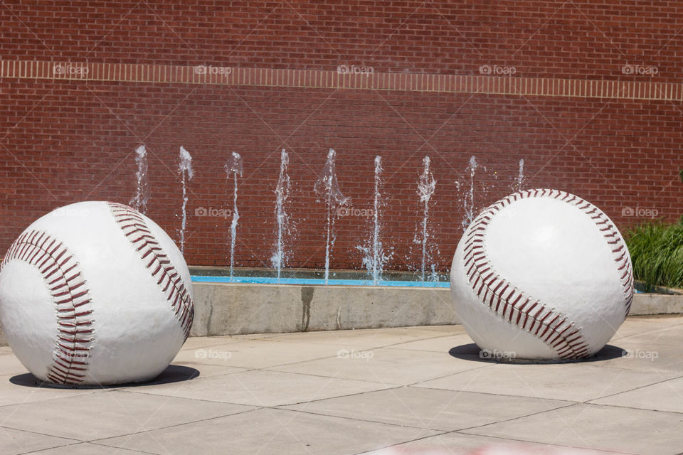Two giant baseballs with water effects and red brick wall in background.