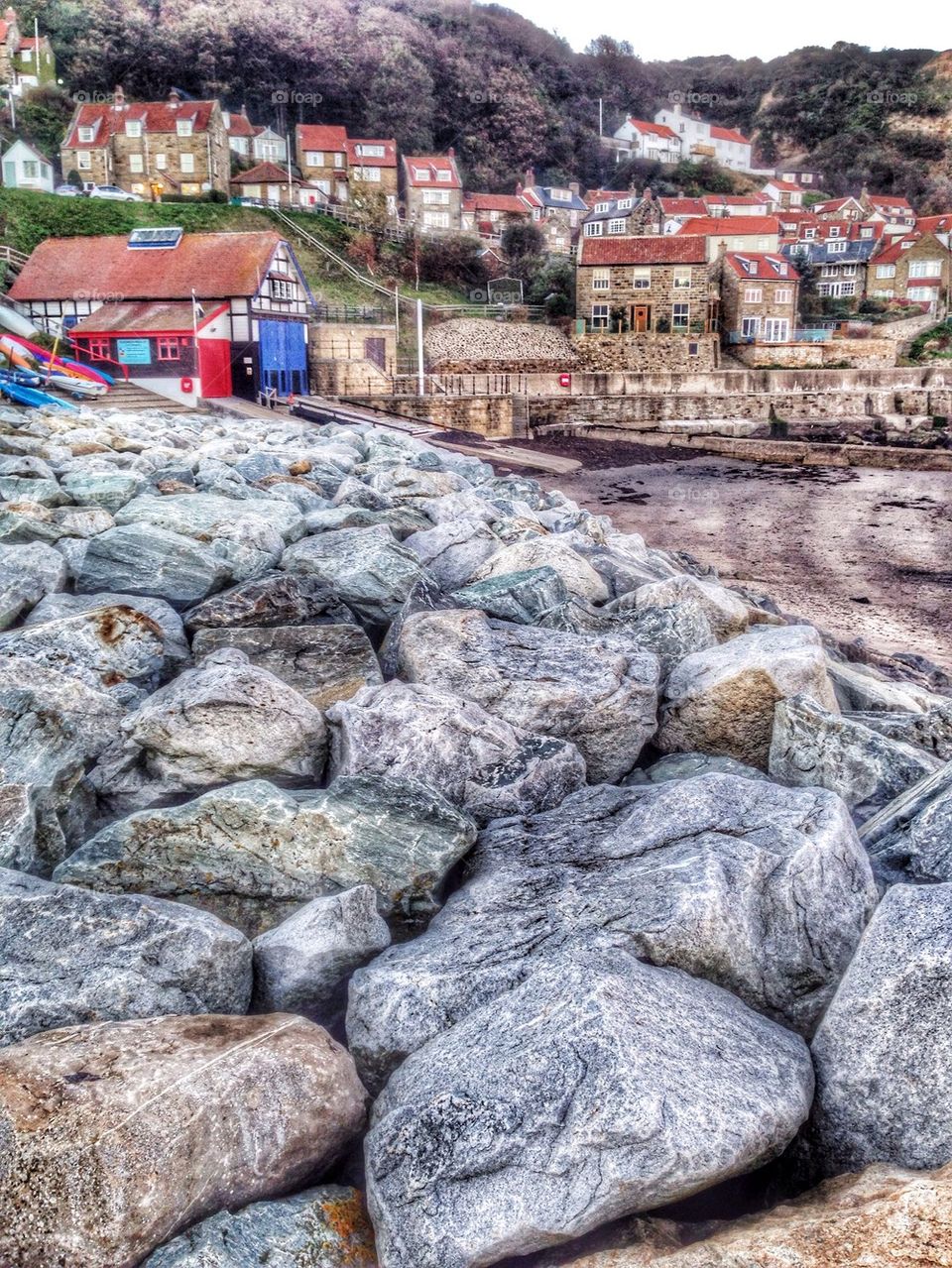 An upright shot of a pretty fishing village with large rocks in the