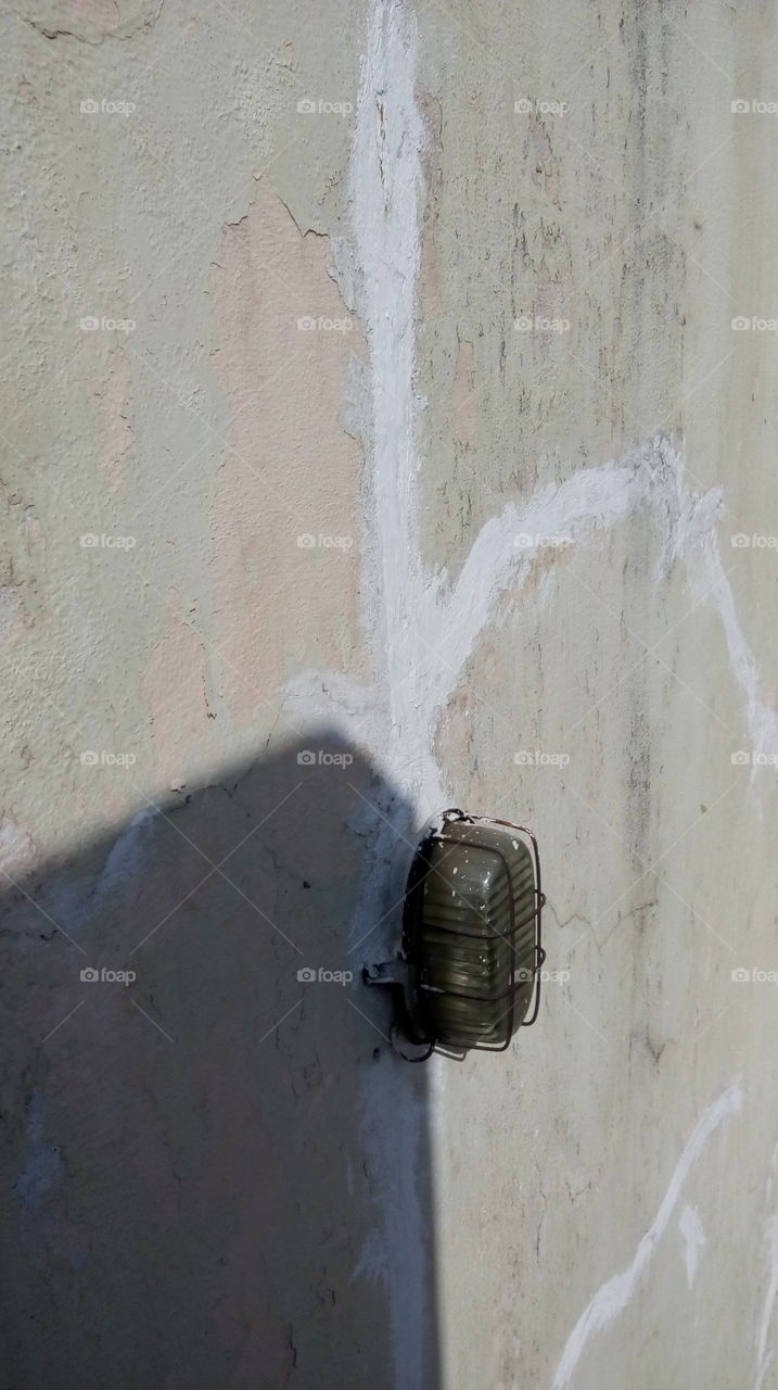 a wall where a old or damaged bulb is placed on it and in the wall cracks are available, shadow is reflected of near wall.