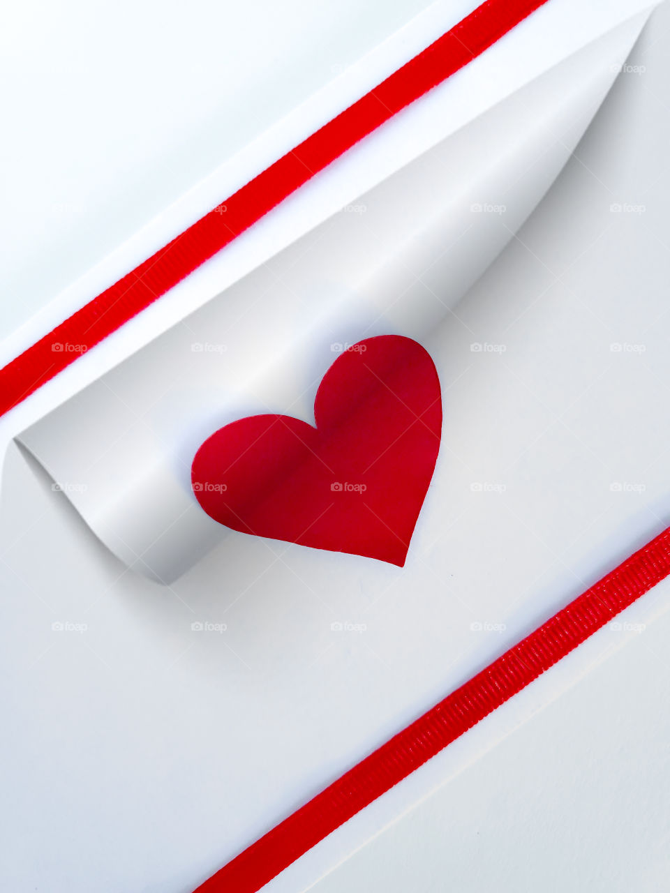 Flat lay concept photo: Turning the page on love.   A white background with two red straight line ribbons and a red heart between.