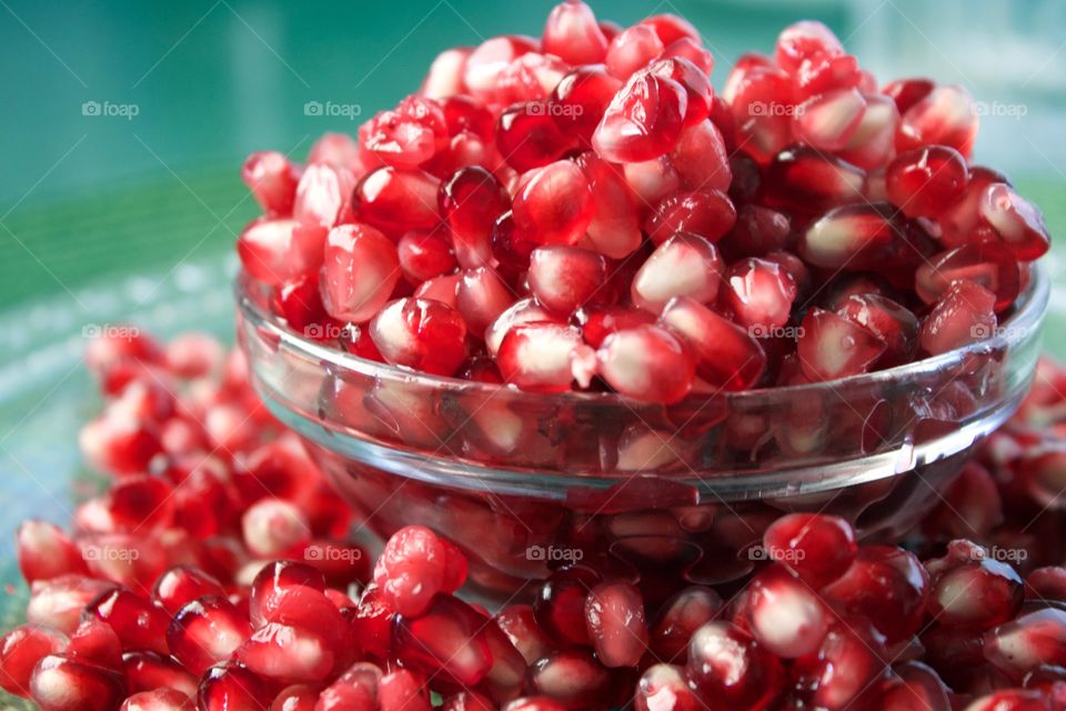 Closeup of fresh pomegranate seeds overflowing a small glass bowl against a green background