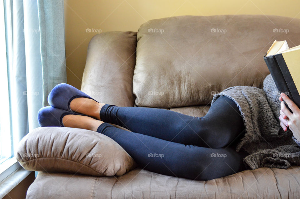 Woman laying on a sofa couch while reading a book