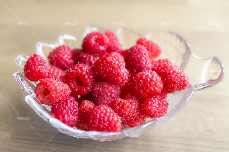 Closeup of a glass bowl filled with fresh delicious raspberries 